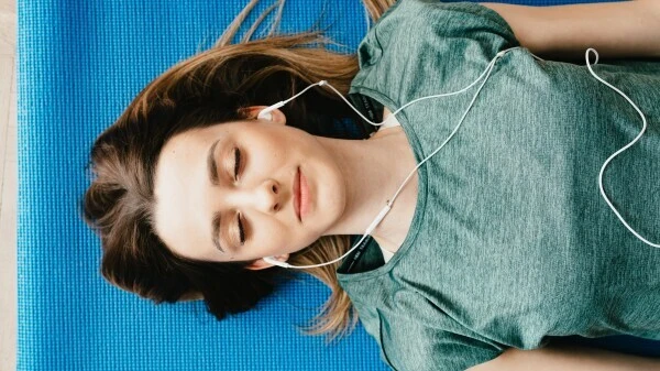 Девојка лежи на простирци за јогу са слушалицама у ушима